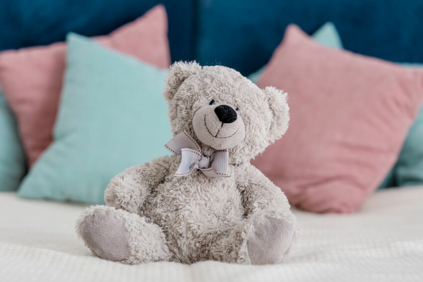 Close up horizontal view of teddy bear sitting on the bed with pillows on background